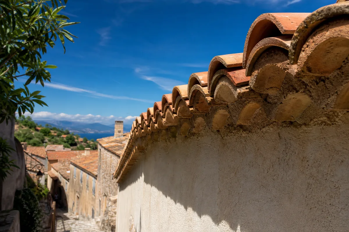 Toits en tuile canal et génoise provençale dans une ruelle du Haut-de-Cagnes sous un ciel bleu